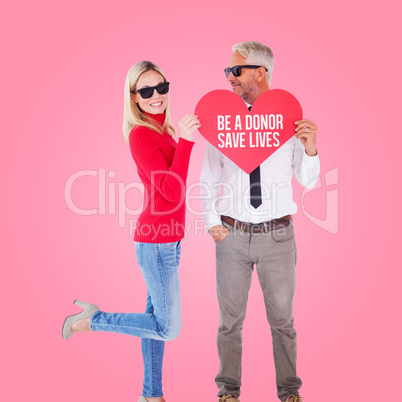 Composite image of cool couple holding a red heart together