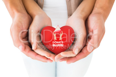 Composite image of couple holding miniature heart in hands