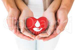 Composite image of couple holding miniature heart in hands