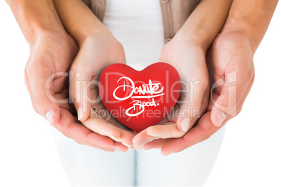 Composite image of couple holding miniature heart in hands