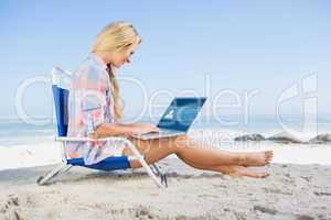 Composite image of woman sitting on beach using her laptop