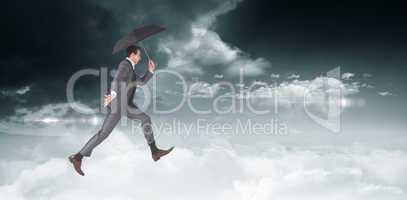 Composite image of businessman jumping holding an umbrella