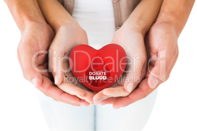 Composite image of couple holding miniature heart in hands