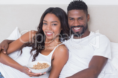 Relaxed couple in bed together eating cereal