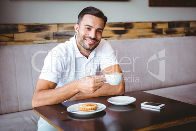 Young man drinking cup of coffee and pastry beside