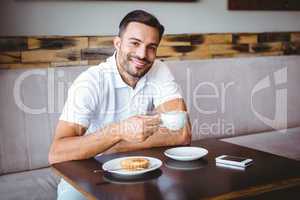 Young man drinking cup of coffee and pastry beside