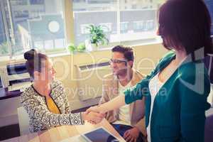 Casual business people shaking hands at desk and smiling