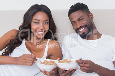 Relaxed couple in bed together eating cereal