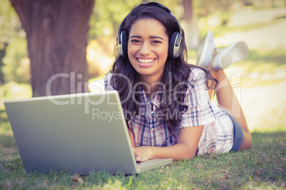 Pretty brunette lying in the grass and using laptop