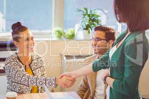 Casual business people shaking hands at desk and smiling