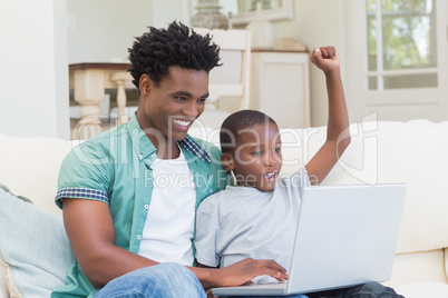Father and son using laptop on the couch