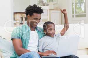 Father and son using laptop on the couch