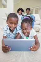 Happy siblings lying on the floor using tablet