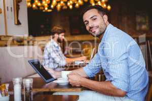 Businessman using tablet while holding cup of coffee