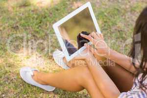 Pretty brunette sitting in the grass and using tablet