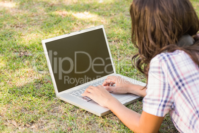 Pretty brunette lying in the grass and using laptop