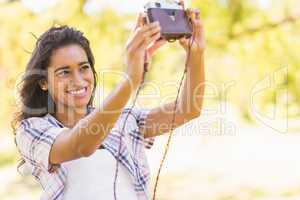 Pretty brunette taking a selfie with retro camera in the park