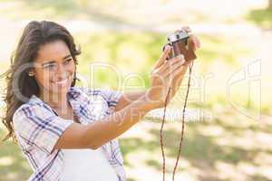 Pretty brunette taking a selfie with retro camera in the park