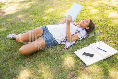 Pretty brunette relaxing in the grass and reading book