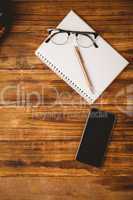 Pen and glasses on notepad next to smartphone