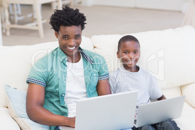 Father and son using laptops on the couch