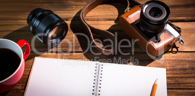 A pen on notepad next to the cup of coffe and camera