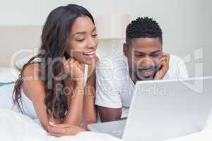 Relaxed couple using laptop on bed