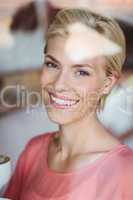 Happy blonde woman smiling at camera and holding a cup of coffee