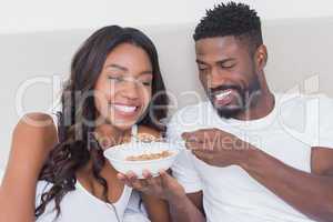 Relaxed couple in bed together eating cereal