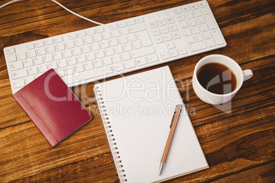 Pen on notepad next to cup of coffee passport and keyboard