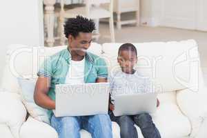 Father and son using laptops on the couch