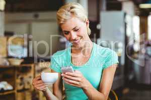 Pretty blonde woman using her smartphone with a cup of coffee