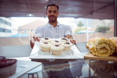 Smiling worker holding cupcakes behind the counter