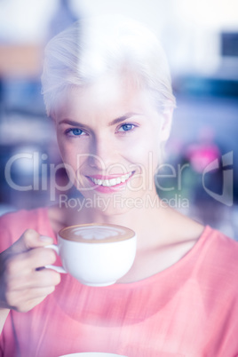 Happy blonde woman smiling at camera and holding a cup of coffee