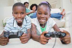 Happy siblings lying on the floor playing video games