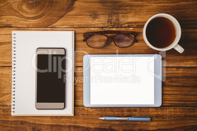 Smartphone on notepad next to tablet and glasses and cup of coff
