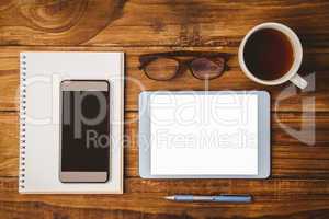 Smartphone on notepad next to tablet and glasses and cup of coff
