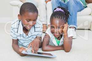 Happy siblings lying on the floor using tablet