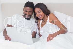 Relaxed couple using laptop in bed together