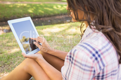 Pretty brunette sitting in the grass and using tablet