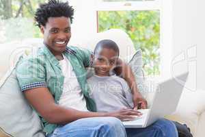 Father and son using laptop on the couch