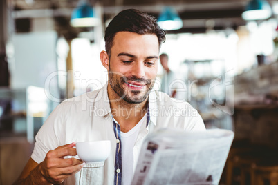 Young man having cup of coffee reading newspaper