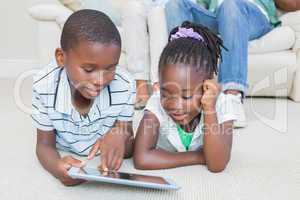 Happy siblings lying on the floor using tablet