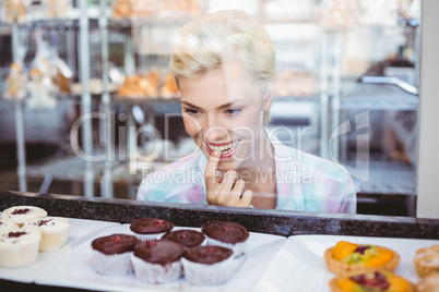 Hesitating pretty woman looking at cup cakes