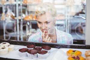 Hesitating pretty woman looking at cup cakes