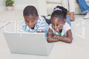 Happy siblings lying on the floor using laptop