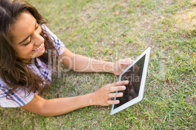 Pretty brunette lying in the grass and using tablet