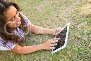 Pretty brunette lying in the grass and using tablet