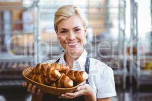 Cheerful gorgeous waitress holding a basket with croissant