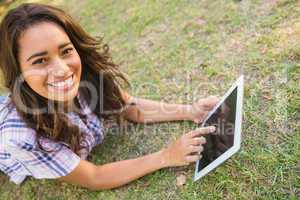 Pretty brunette lying in the grass and using tablet